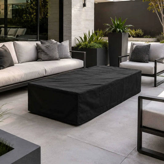 Flame Havens Refuge Series 68 x 30 x 15-inch rectangular GFRC natural gas fire pit protected by a fitted black canvas fabric cover. The covered fire pit is centered within a modern outdoor lounge featuring white cushioned seating, black frames, large planters, and contemporary landscaping.
