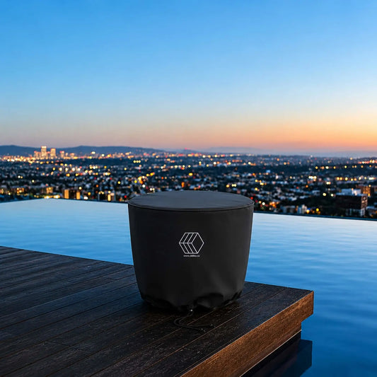 HPC Fire Hearth Products Controls GFRC Concrete Element 20 Round Fire Column Weather Cover Lifestyle 1 featuring a covered round fire column positioned on a luxury infinity-edge pool deck overlooking a panoramic city skyline at sunset. The black fitted weather cover protects the fire feature while blending seamlessly into the upscale outdoor living space. The image highlights year-round protection, premium outdoor design, and weather-resistant storage for modern fire column installations.