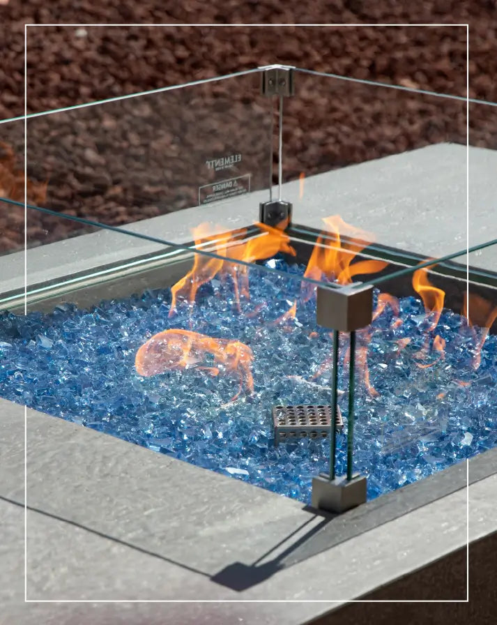 Modern outdoor fire pit with vibrant blue fire glass and a protective glass wind guard, enhancing style and safety for any patio space.