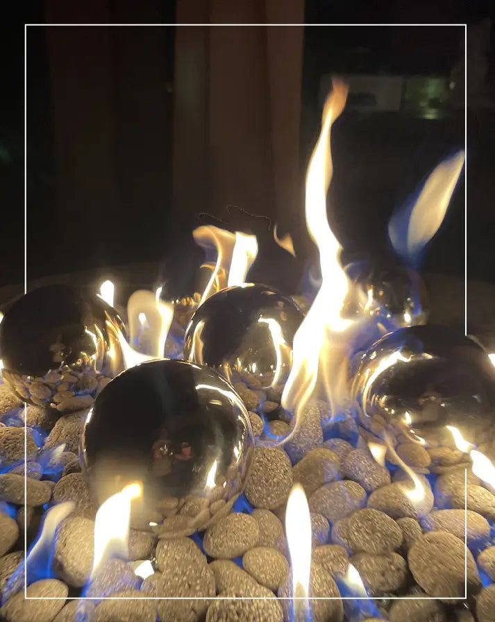 Reflective fire balls with smooth ceramic pebbles in a contemporary gas fire pit, creating a stunning and modern outdoor ambiance.