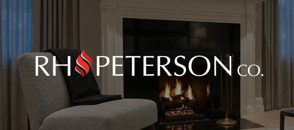 A living room scene with a gray upholstered armchair in the foreground, a fireplace with a visible fire and dark surround in the background, and a large overlaid RH PETERSON co. logo across the center.