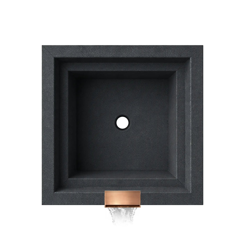 Top-down view of the graphite Serenity Series square ripple water bowl showing the empty basin interior and centered drain opening. The stepped square interior walls and textured graphite finish highlight the clean geometric design, while the copper spillway opening is visible at the front edge where water exits the bowl to create a decorative waterfall feature.