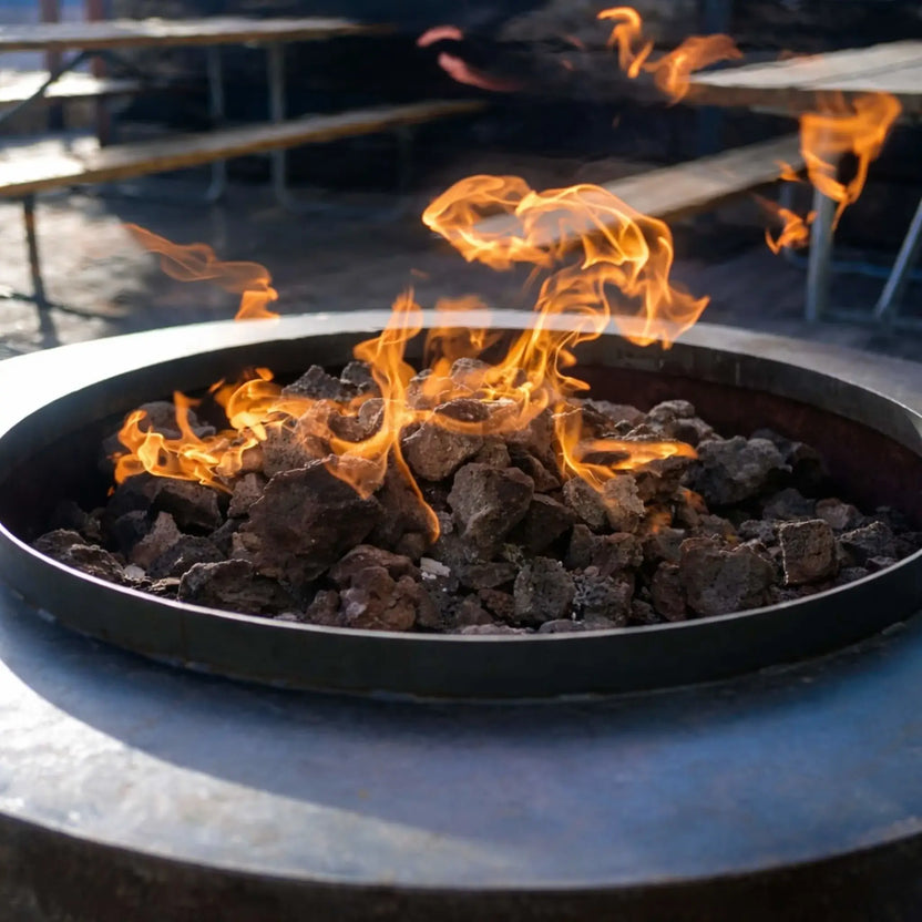 Close-up of a circular stone fire pit packed with oversized XXL lava rock, vibrant flames weaving through the porous volcanic stones in a cozy nighttime backyard lounge.