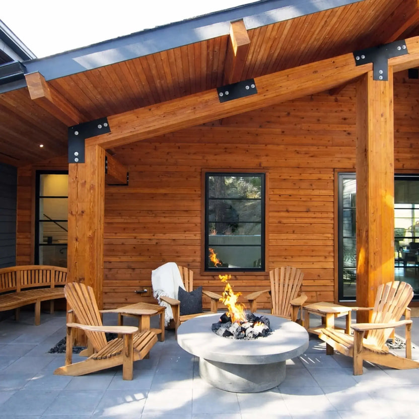 Contemporary round steel fire bowl filled with extra extra large lava rock, bright orange flames rising dramatically with outdoor seating blurred in the background.
