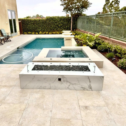 Contemporary backyard fire pit with a linear rectangular burner protected by a tempered glass wind guard, positioned near a swimming pool and spa, blending fire and water elements in a luxury outdoor living space.