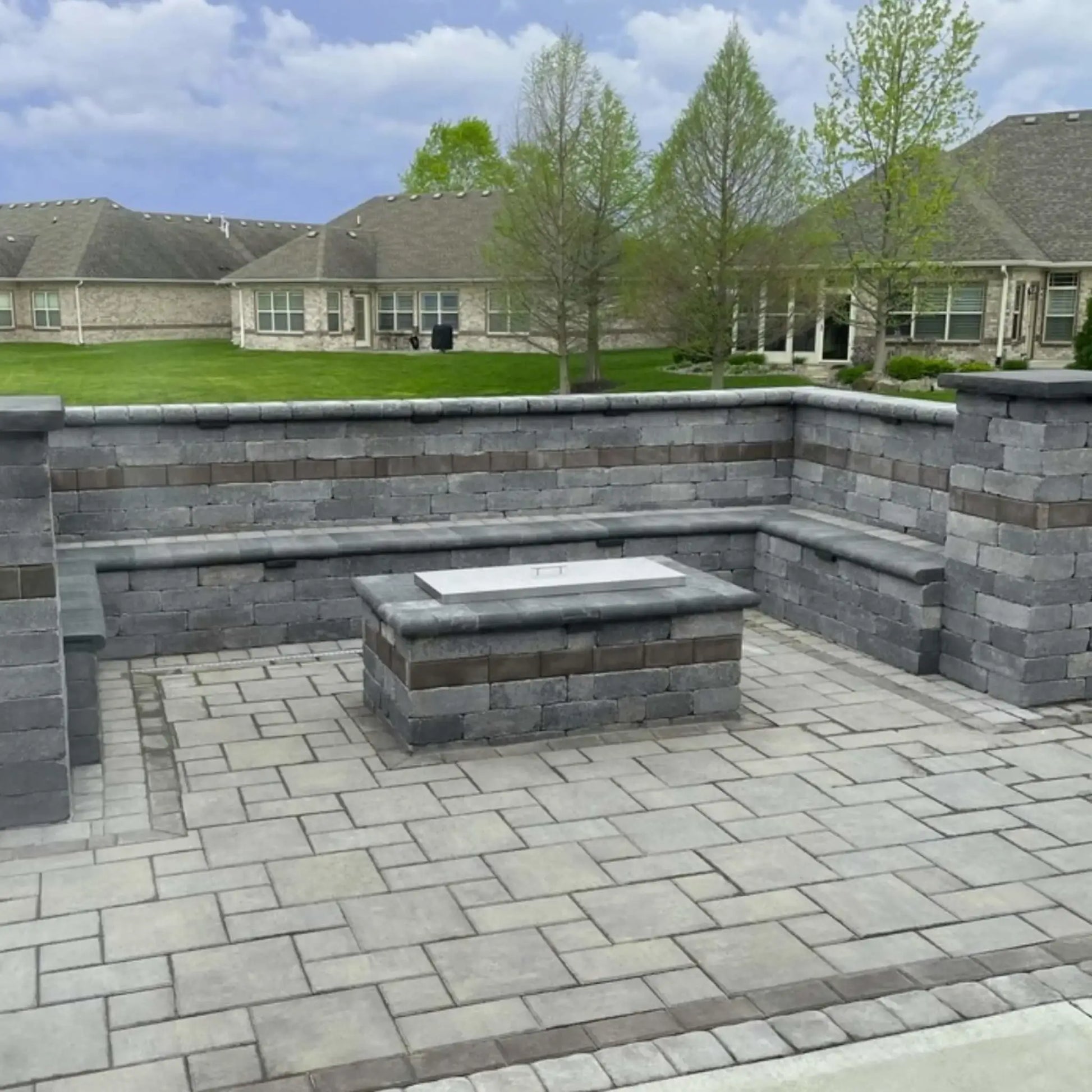 Rectangular stainless steel fire pit burner cover installed on a modern stone fire feature, offering a clean brushed finish that converts the fire pit into a usable tabletop.