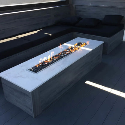 Backyard fire pit built with natural stone walls and a stainless steel linear burner pan, producing a clean ribbon of flame set against a landscaped garden and outdoor seating area.