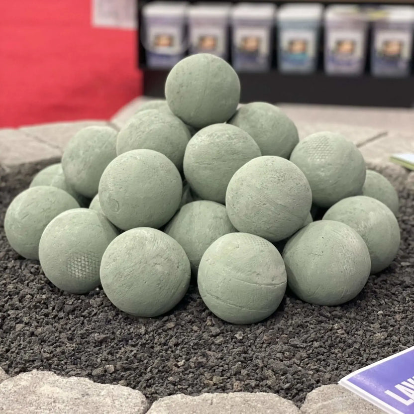Cape Grey 4 inch lite stone fire balls stacked inside an outdoor fire pit display, showing a pyramid arrangement of textured concrete spheres resting on dark lava rock media in a patio showroom setting.