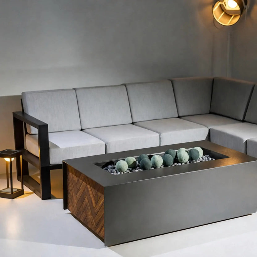 Close view of a modern fire pit table with bright flames dancing above round fire balls set in a bed of small stones, showing the textured surfaces and warm glow.