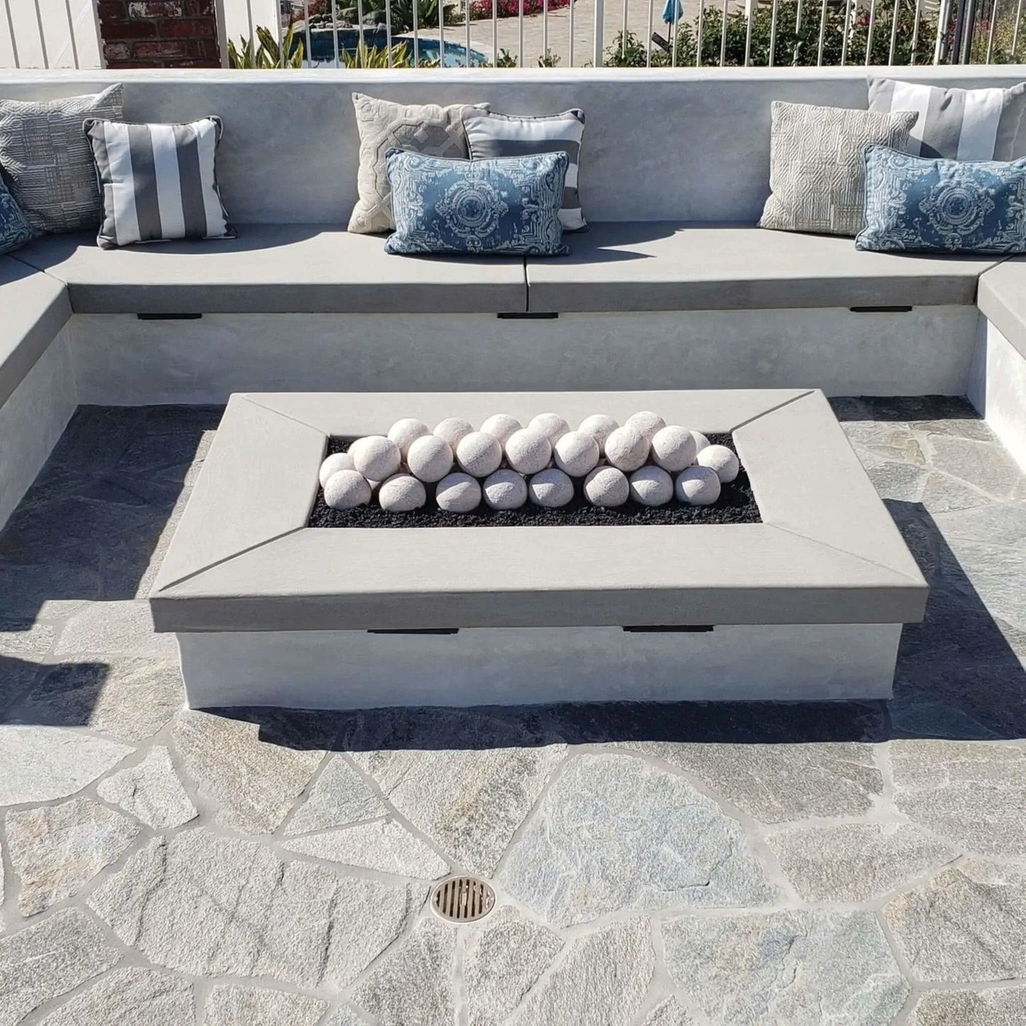 Sunken patio lounge with a large concrete fire table; Cottage White Lite Stone fire balls arranged in rows over black lava rock in the center burner, surrounded by a gray outdoor sectional and accent pillows.