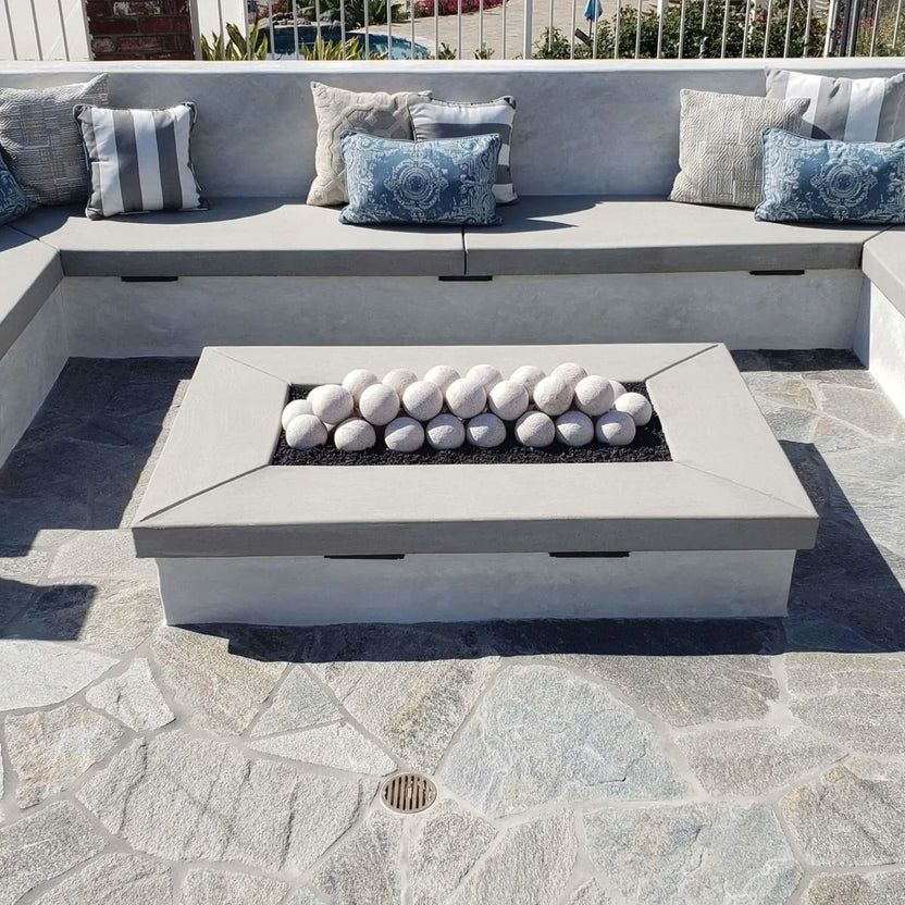 Sunken patio lounge with a large concrete fire table; Cottage White Lite Stone fire balls arranged in rows over black lava rock in the center burner, surrounded by a gray outdoor sectional and accent pillows.