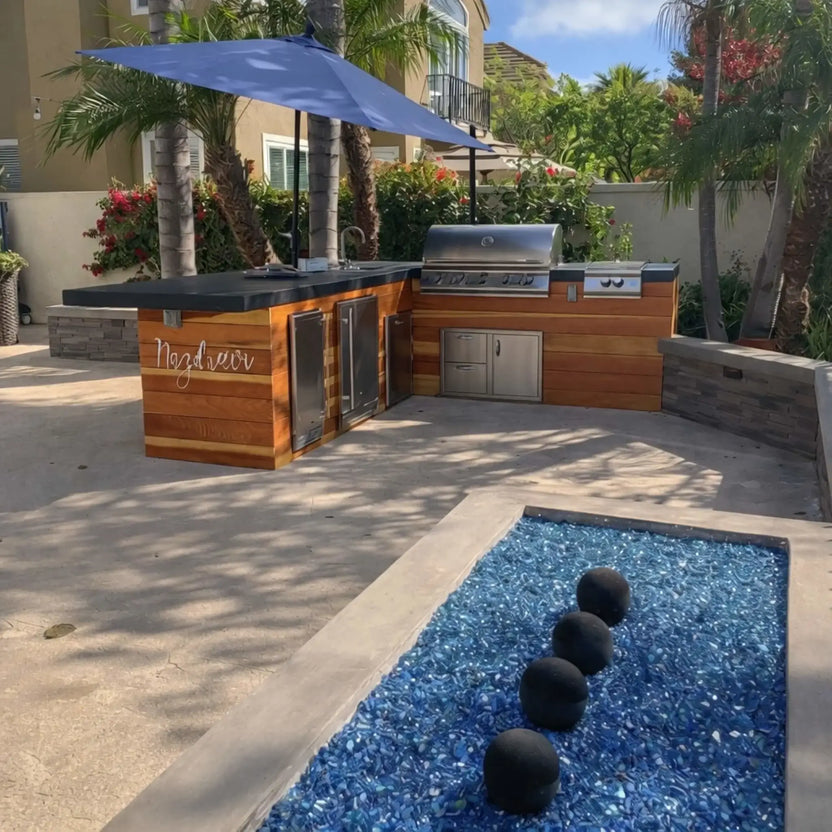 Rectangular outdoor fire table burning with tall yellow flames over mixed fire media, highlighting round Cape Grey fire balls placed among smaller stones in the burner pan.