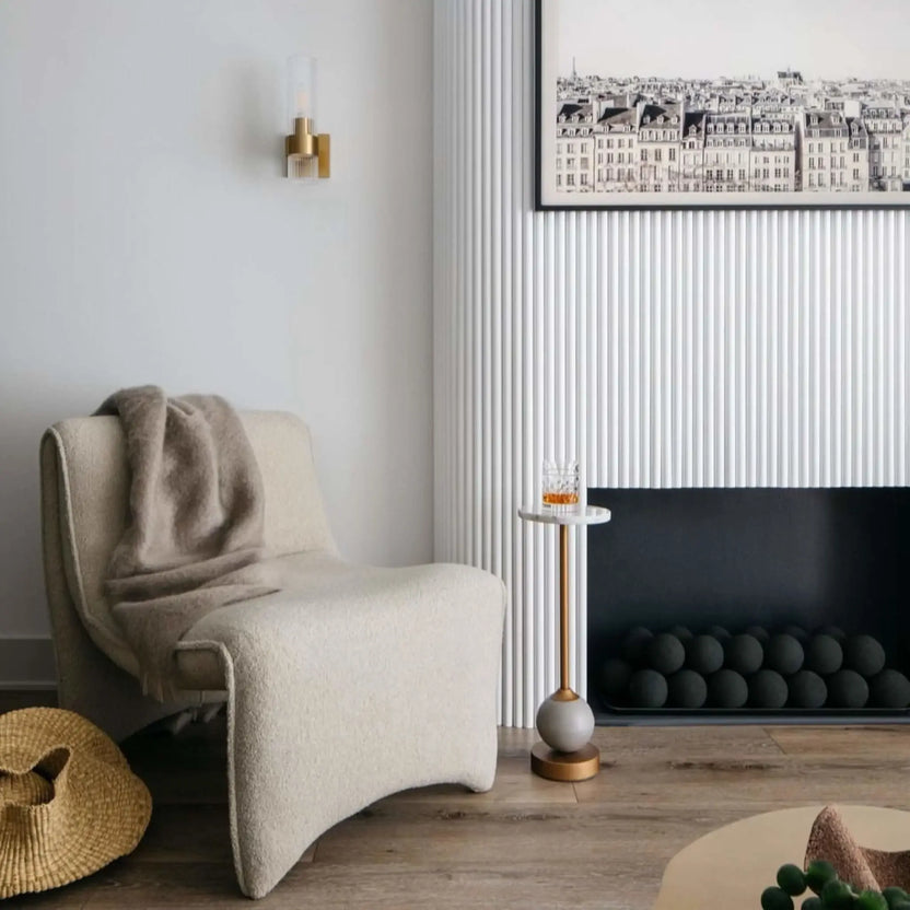 Minimal modern living room with a low, wide black fireplace insert filled with matte black fire balls, styled with a sculptural lounge chair, wall sconce, and framed artwork.