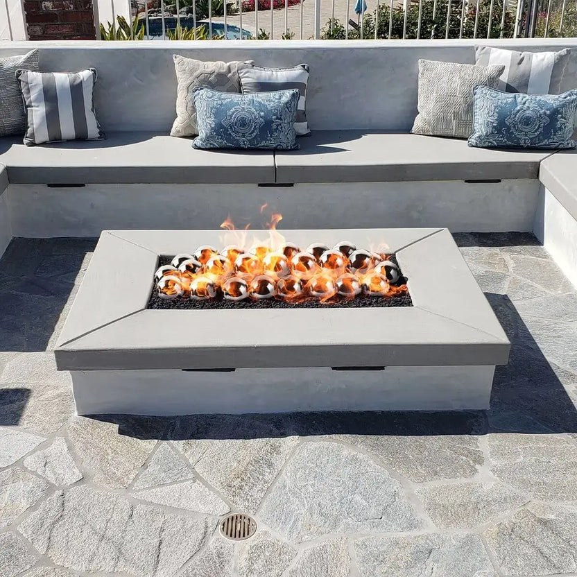 Modern outdoor fire table with stainless steel fire balls arranged in a linear burner, set in a light gray concrete fire feature surrounded by contemporary patio seating.