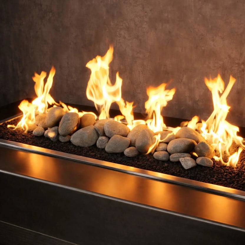 Outdoor gas fire feature burning with bright, natural flames over Cape Gray Lite Stones by American Fire Products, showing smooth gray fire stones arranged across a linear burner for a modern patio design.