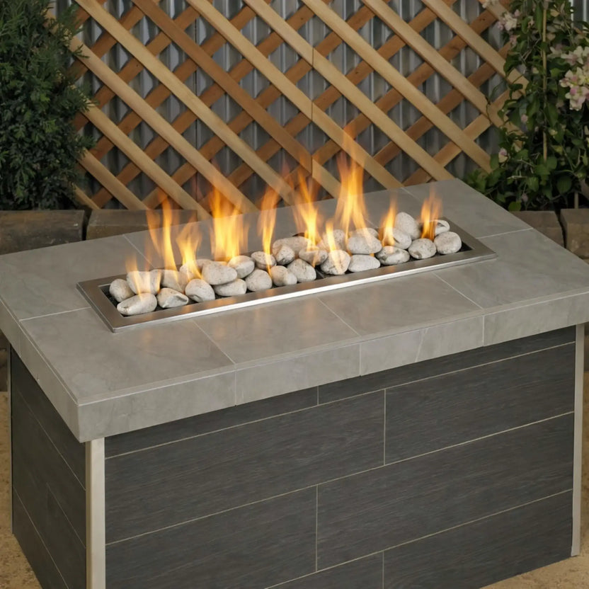 Outdoor linear gas fire table burning with tall yellow flames over Cottage White Lite Stones by American Fire Products, highlighting the bright stone color and clean modern fire pit design.