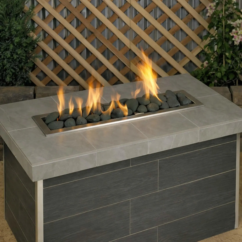 Modern outdoor linear gas fire table burning with tall flames over Matte Black Lite Stones by American Fire Products, highlighting the contrast between dark fire stones and bright yellow flames.