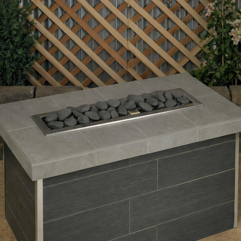 Rectangular outdoor gas fire table filled with Thunder Gray Lite Stones by American Fire Products, shown without flames to highlight the smooth stone arrangement, deep gray tones, and clean modern fire pit layout.