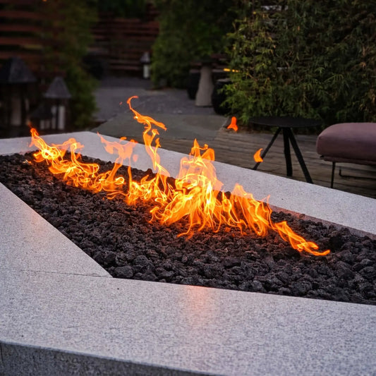 Custom linear rectangular fire pit burner bed filled with medium black lava rock, creating a long ribbon flame feature in a sleek outdoor patio design.