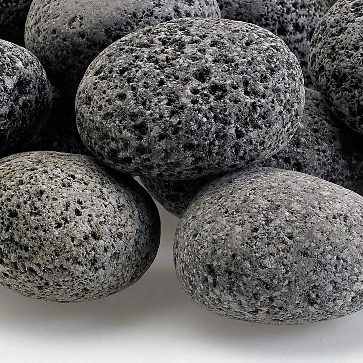 Detailed close-up of medium lava rocks showing their rugged, pitted volcanic surface, natural gray color variation, and textured finish designed for even heat distribution in fire features.