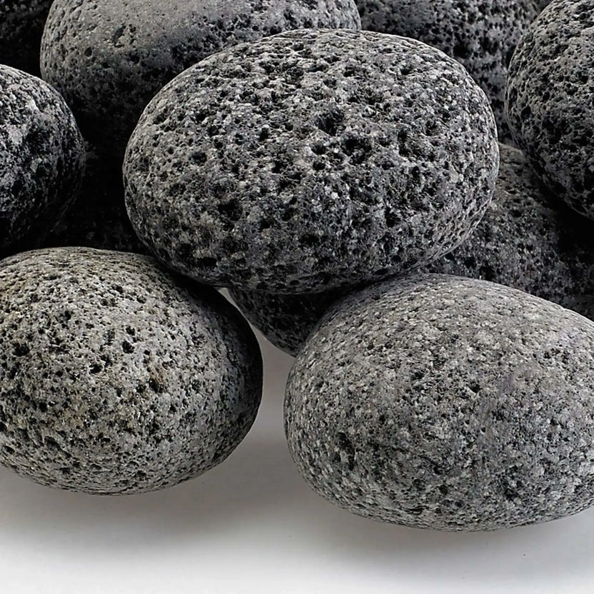 Detailed close-up of medium lava rocks showing their rugged, pitted volcanic surface, natural gray color variation, and textured finish designed for even heat distribution in fire features.