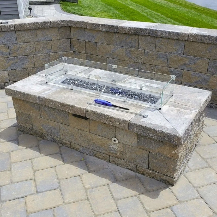 Built in stone fire pit with glass wind guard and fire glass media, photographed during installation, illustrating the use of a polished chrome universal gas key for operating the gas control valve.