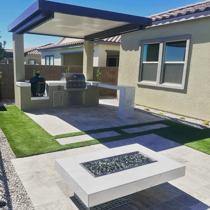 Contemporary backyard with a covered outdoor kitchen pavilion, built-in grill station, and a rectangular fire pit table featuring a drop-in burner pan filled with fire glass, surrounded by clean concrete walkways and artificial turf.