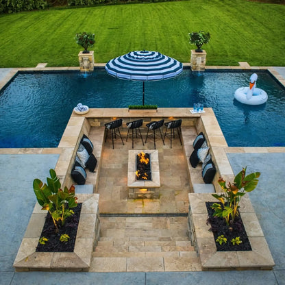 Luxury backyard entertaining area featuring a sunken patio with built-in seating, a rectangular fire pit with drop-in burner pan, and a swimming pool framed by stonework and landscaping.