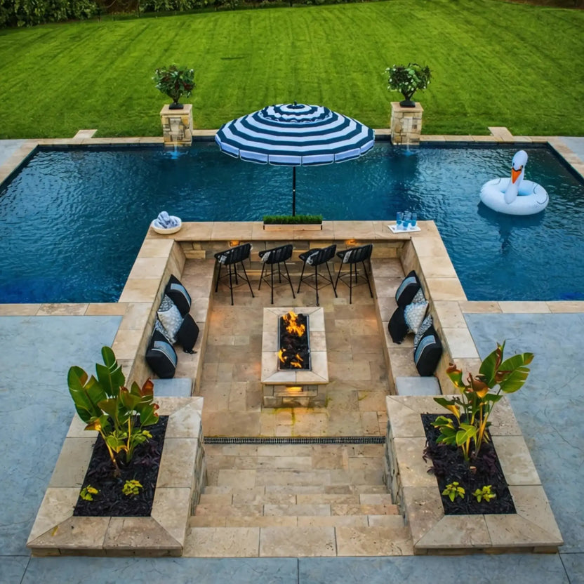 Luxury backyard entertaining area featuring a sunken patio with built-in seating, a rectangular fire pit with drop-in burner pan, and a swimming pool framed by stonework and landscaping.