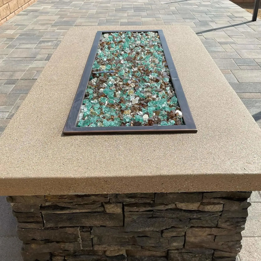 Close-up view of a rectangular fire pit burner pan filled with mixed fire glass, set flush into a textured stone top, highlighting the pan’s straight edges and centered installation.