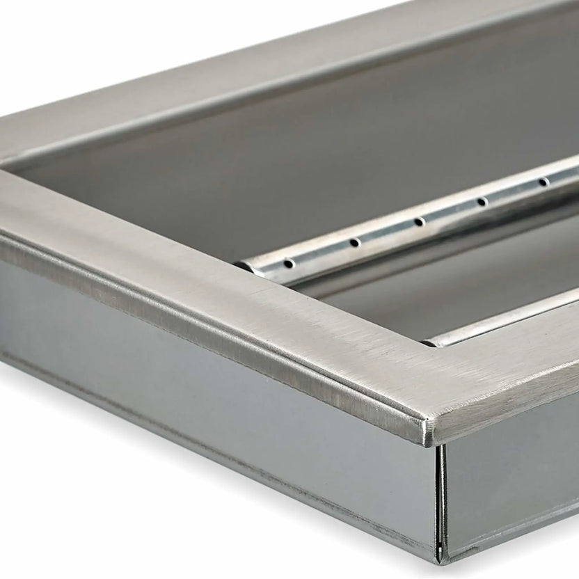 Angled close-up of a stainless steel fire pit pan showing the interior burner rail, reinforced pan walls, and smooth brushed steel surface used in outdoor fire pit systems.