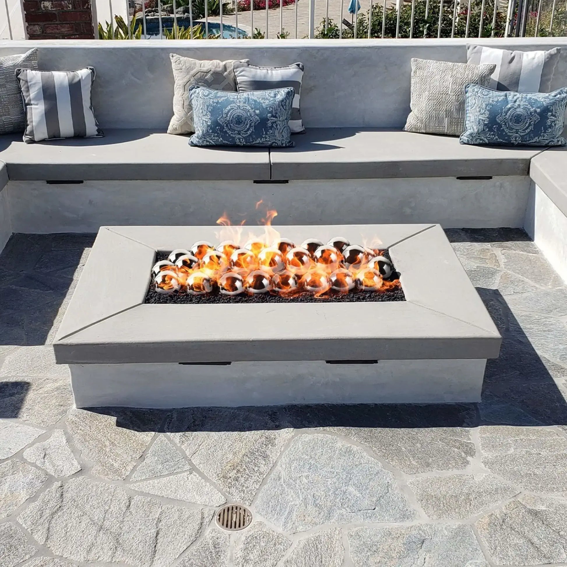 Linear rectangular fire pit with a flat burner pan producing tall flames through bronze-toned fire glass, integrated into a stacked stone bench wall in a landscaped backyard setting.