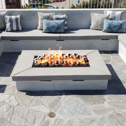 Linear rectangular fire pit with a flat burner pan producing tall flames through bronze-toned fire glass, integrated into a stacked stone bench wall in a landscaped backyard setting.