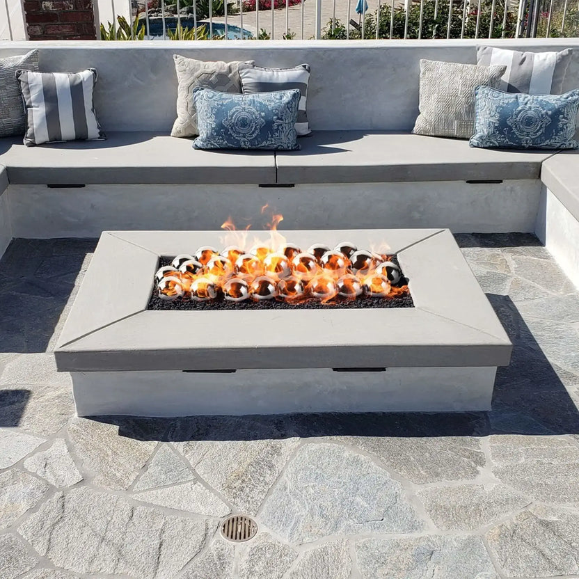 Linear rectangular fire pit with a flat burner pan producing tall flames through bronze-toned fire glass, integrated into a stacked stone bench wall in a landscaped backyard setting.