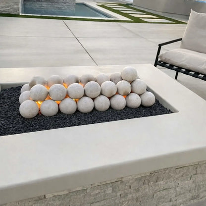 Modern rectangular fire pit table featuring a flat burner pan with decorative fire spheres over black lava rock, set within a sleek outdoor patio design with minimalist seating and light stone finishes.