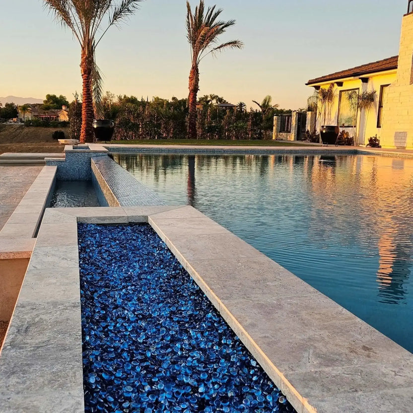 Contemporary outdoor lounge with a long rectangular fire pit table featuring a flat burner pan and decorative fire media, surrounded by woven patio furniture and wood decking.