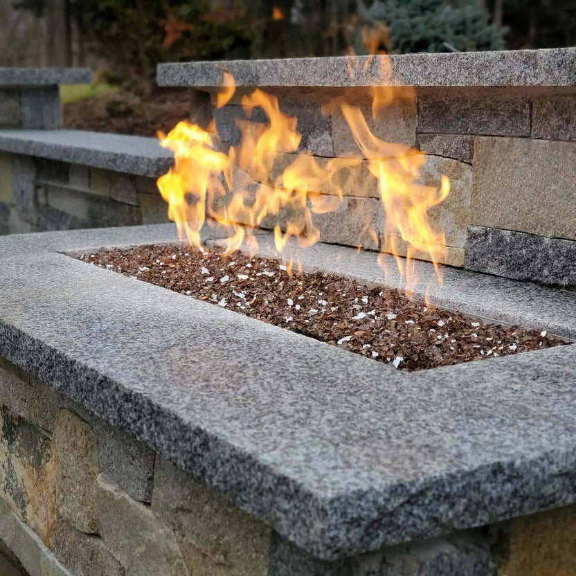 Linear fire feature built into a stone bench wall, showcasing a flat stainless steel burner pan with active flames and fire glass, designed for modern outdoor living spaces.