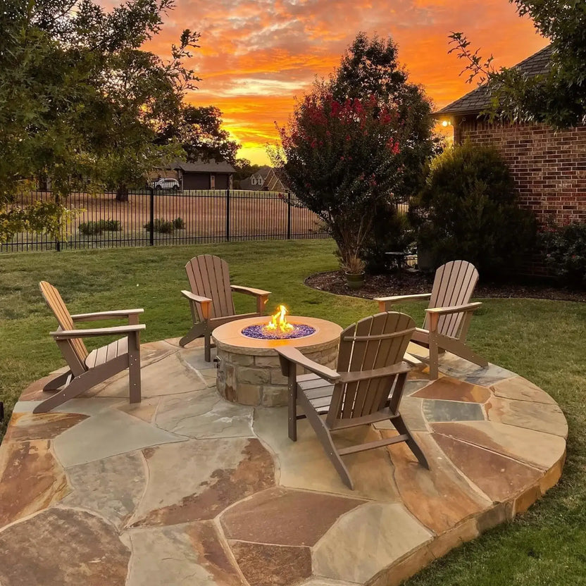 Backyard fire pit seating area with a round stainless steel drop-in fire pit pan burning over cobalt blue fire glass, surrounded by outdoor chairs at sunset for a warm gathering space.