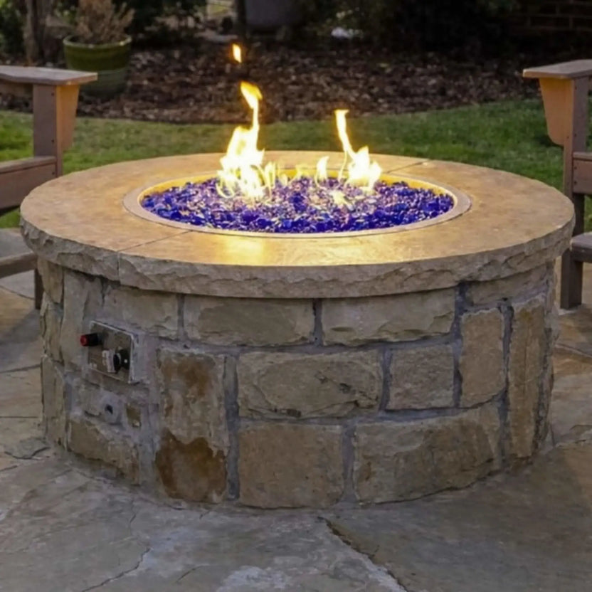 Outdoor stone fire pit featuring a round stainless steel fire pit pan filled with cobalt blue fire glass, creating a vibrant flame presentation in a landscaped backyard setting.
