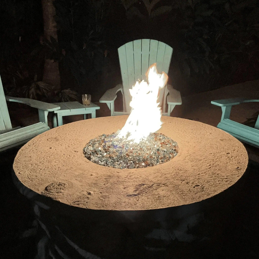 Evening patio fire pit with tall flames rising from multicolored fire glass, centered among Adirondack chairs for a cozy outdoor seating area at night.