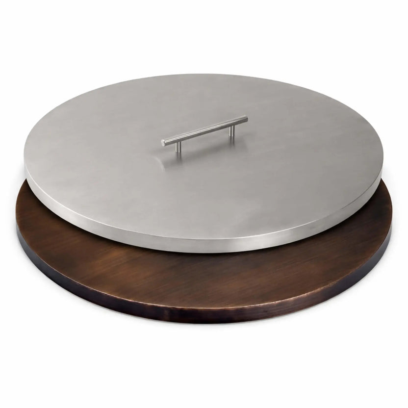 Side-by-side comparison of round stainless steel and oil rubbed bronze fire pit burner covers, highlighting the contrast between brushed silver and dark bronze finishes, each with a centered low-profile handle.