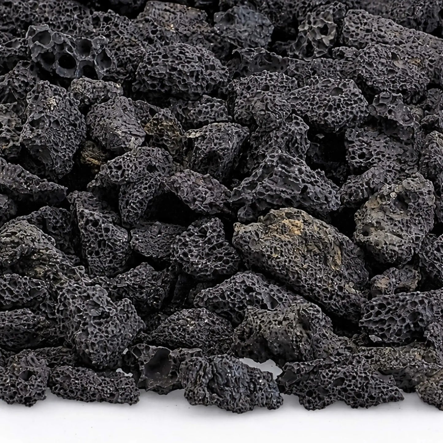 Close-up detail of small lava rocks showing rugged, porous volcanic texture and charcoal-black coloring, commonly used to improve gas flow and heat distribution in fire pit burners.