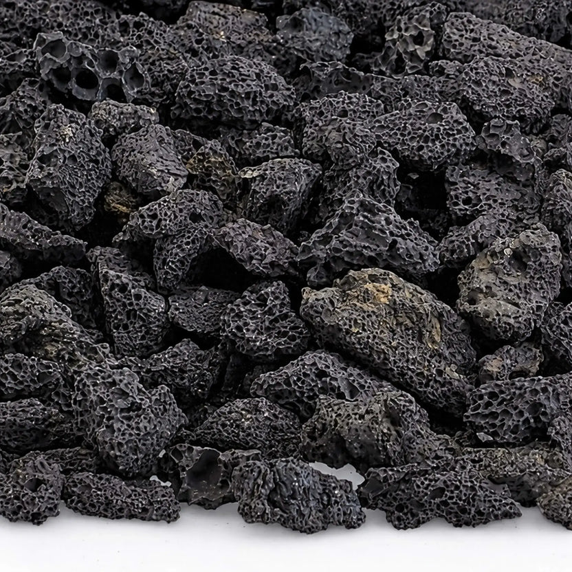 Close-up detail of small lava rocks showing rugged, porous volcanic texture and charcoal-black coloring, commonly used to improve gas flow and heat distribution in fire pit burners.