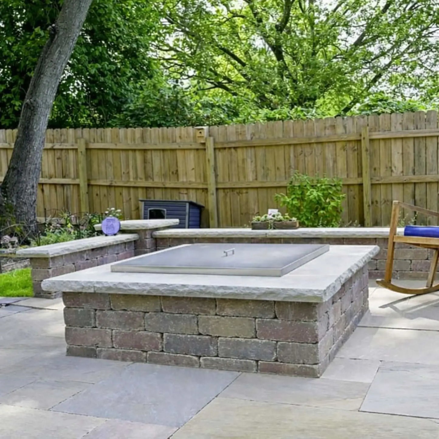 Outdoor patio fire pit with a square stainless steel burner cover installed, sitting flush within a stone fire pit enclosure to protect the burner while maintaining a clean, finished appearance.