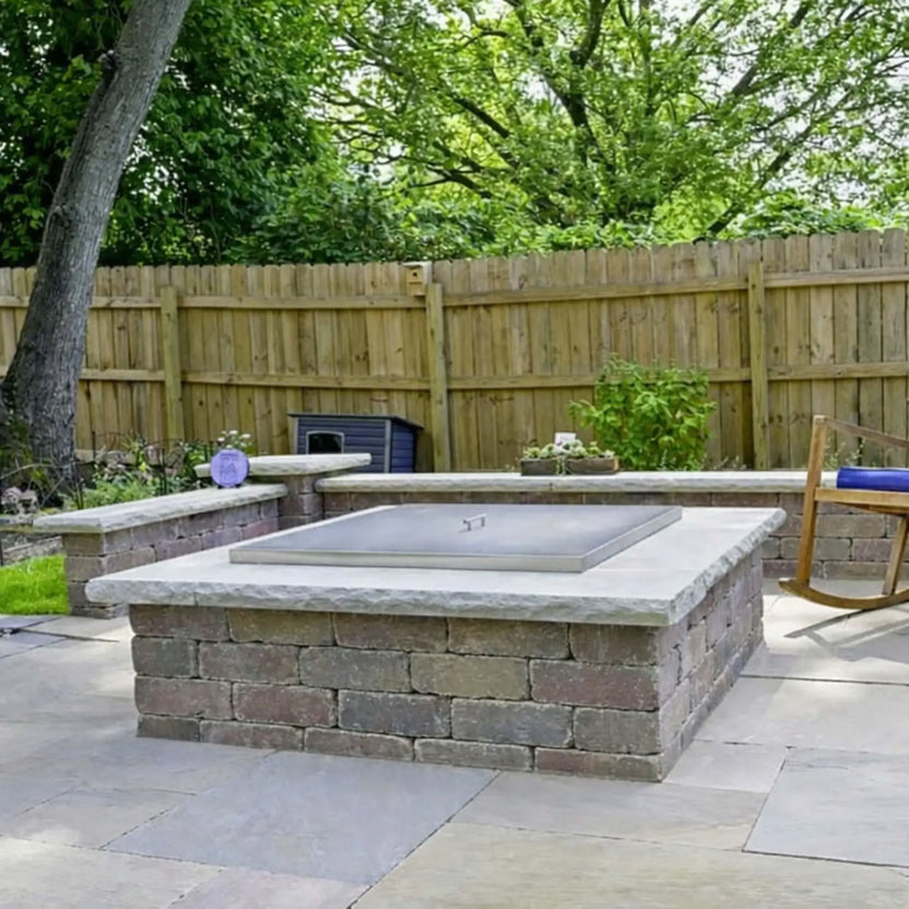 Outdoor patio fire pit with a square stainless steel burner cover installed, sitting flush within a stone fire pit enclosure to protect the burner while maintaining a clean, finished appearance.