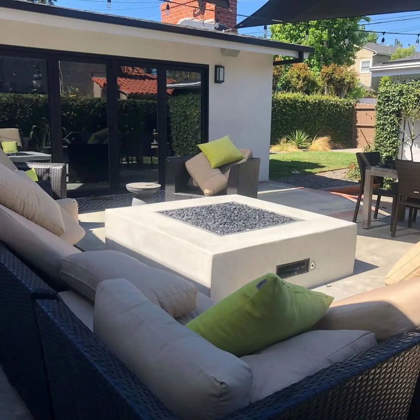 Contemporary backyard patio featuring a square fire pit table with a stainless steel burner pan and dark fire glass, surrounded by outdoor lounge seating and a shaded pergola.
