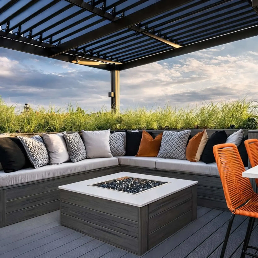 Symmetrical outdoor seating area centered around a square fire pit with a stainless steel drop-in burner pan, illuminated by soft landscape lighting on a stone patio.