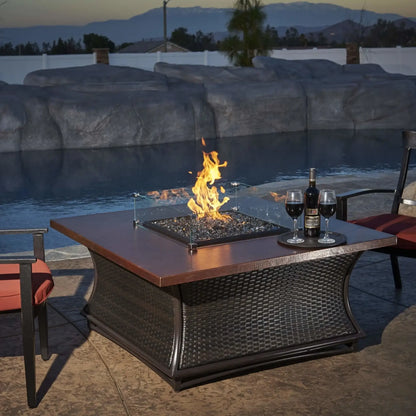 Square tempered glass wind guard installed on a modern outdoor fire table, surrounding a lit fire feature and blending seamlessly with patio furniture in a backyard setting.