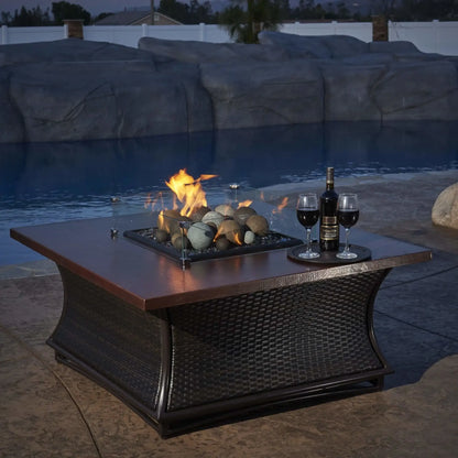 Outdoor fire pit table featuring a square glass wind guard enclosing decorative fire media, shown in a stylish patio environment with seating and evening ambiance.