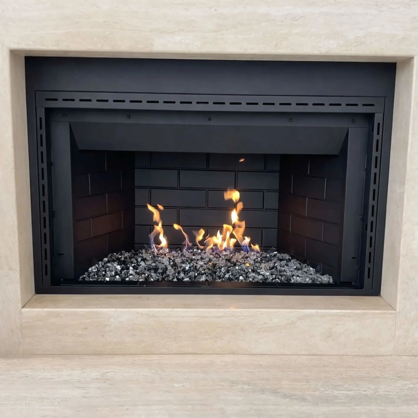 Built-in gas fireplace with a stainless steel H burner and mixed fire glass, showing steady flames rising across the burner bed inside a clean black metal firebox framed by light natural stone for a contemporary residential installation.